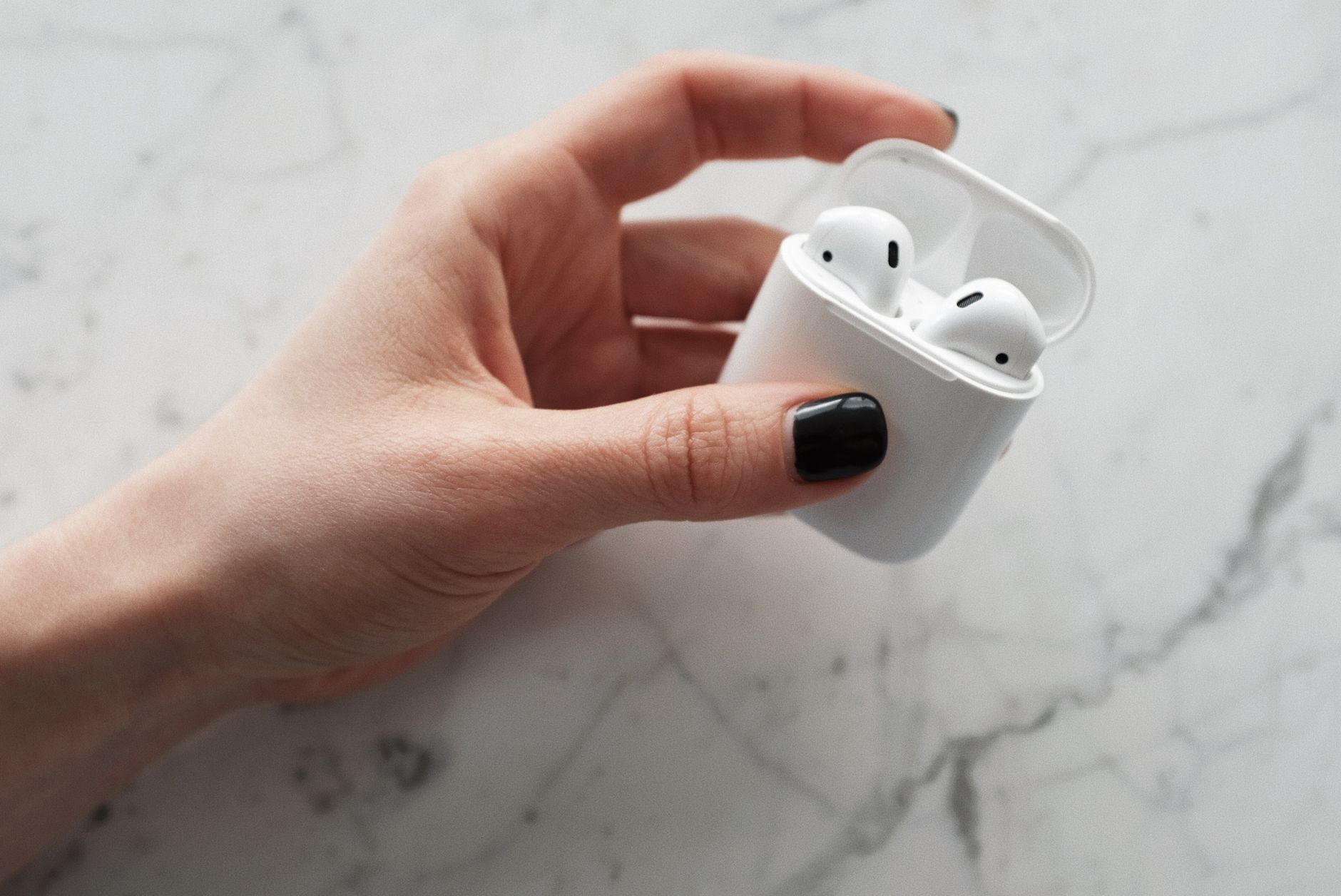 A person holding an open white AirPods charging case in their hand, showing the status light indicator