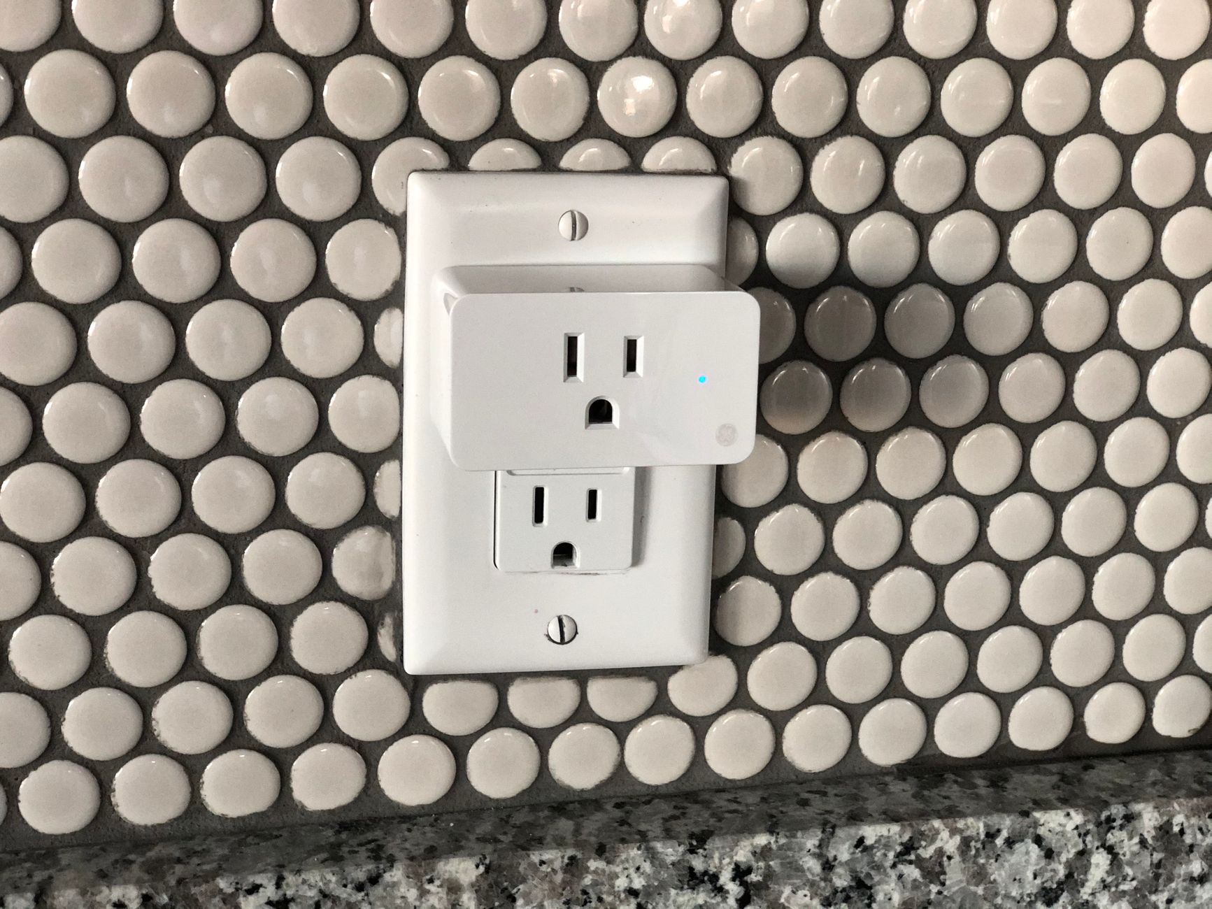 A person plugging a compact smart plug into a white dual wall socket.